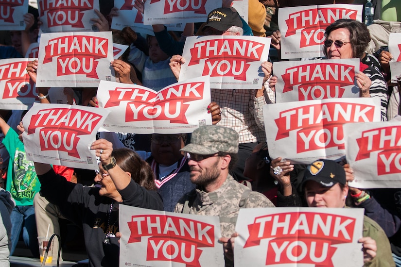 Crowd holds up several thank you signs.