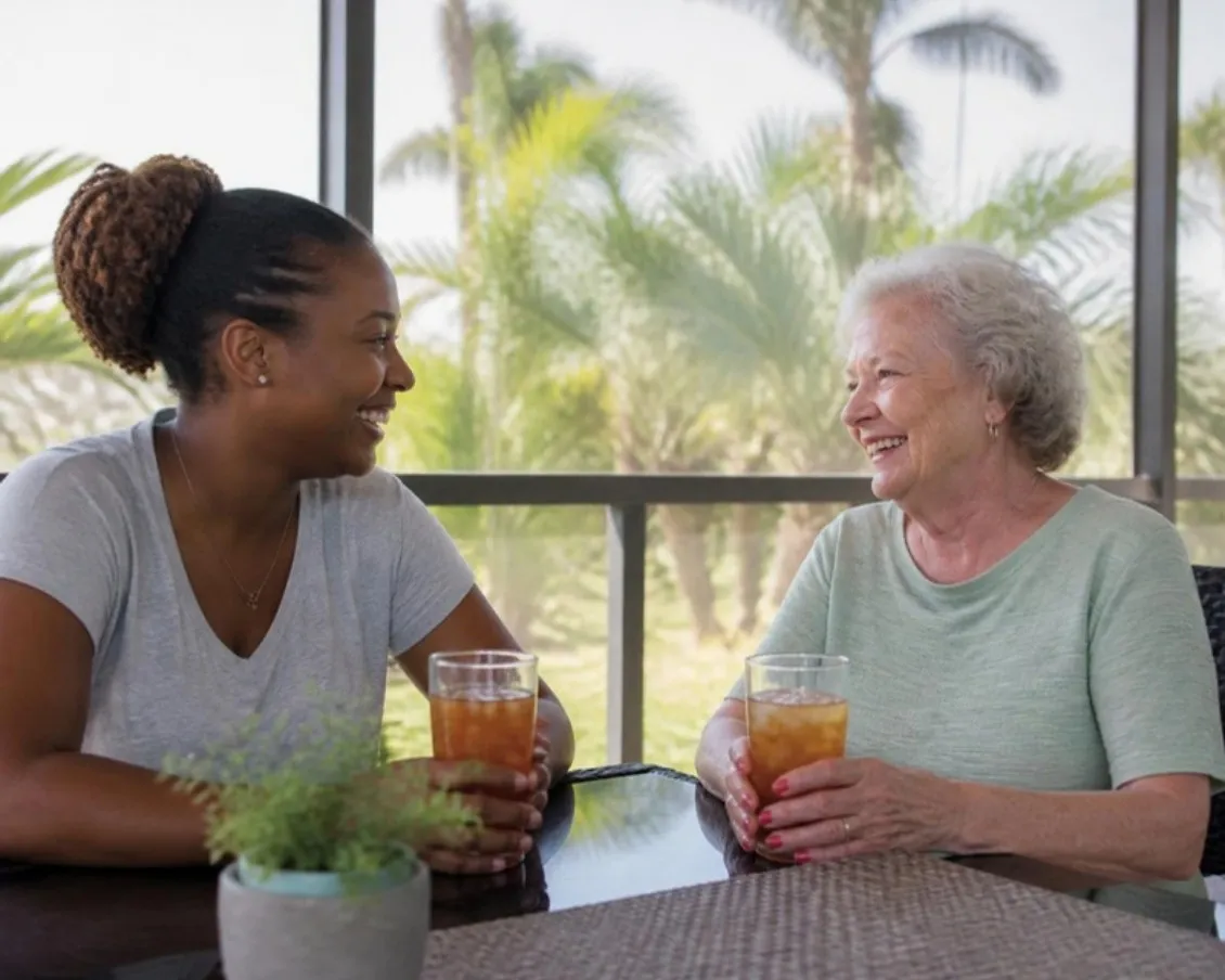 Private caregiver sharing iced tea and conversation with an older woman on a Florida lanai