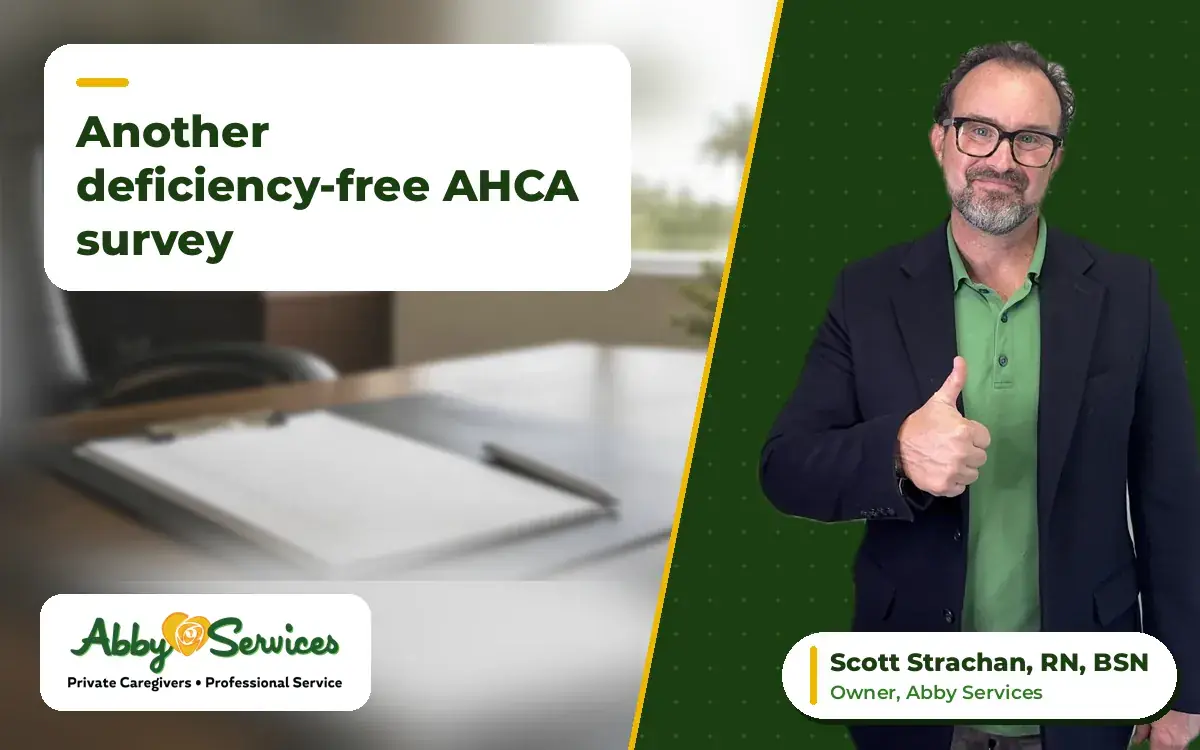 Scott Strachan, RN, BSN, owner of Abby Services, giving a thumbs up, with an office desk with a clipboard checklist, a pen and a potted plant in the background