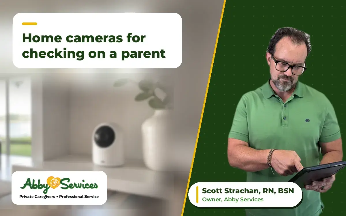 Scott Strachan, RN, BSN, owner of Abby Services, using a tablet, with a small home security camera on a living room bookshelf in the background