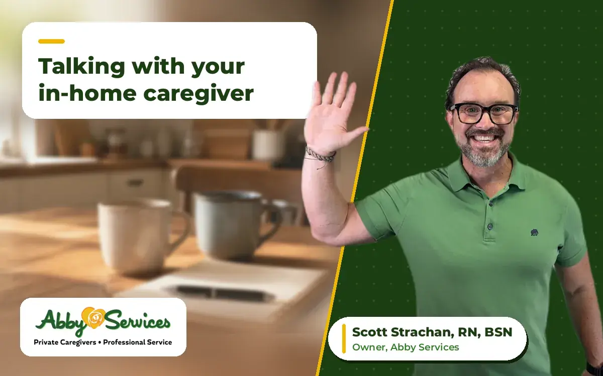 Scott Strachan, RN, BSN, owner of Abby Services, waving hello, with two coffee mugs and a notepad on a kitchen table in the background